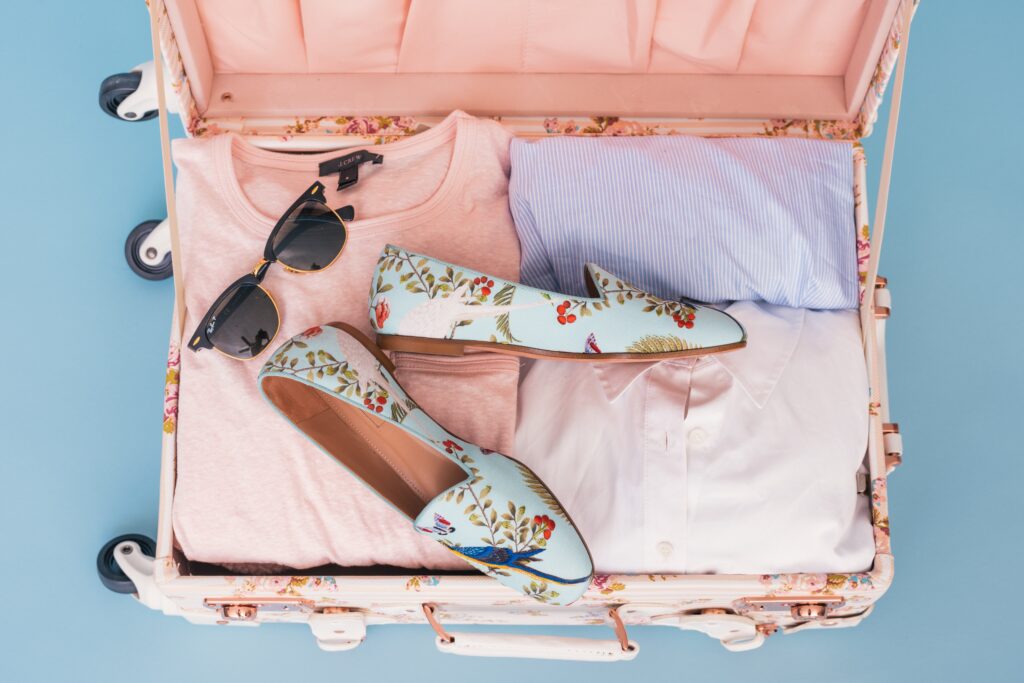 pink suitcase filled with clothes, sunglasses, shoes. Compression packing cubes could help stop an overflowing suitcase