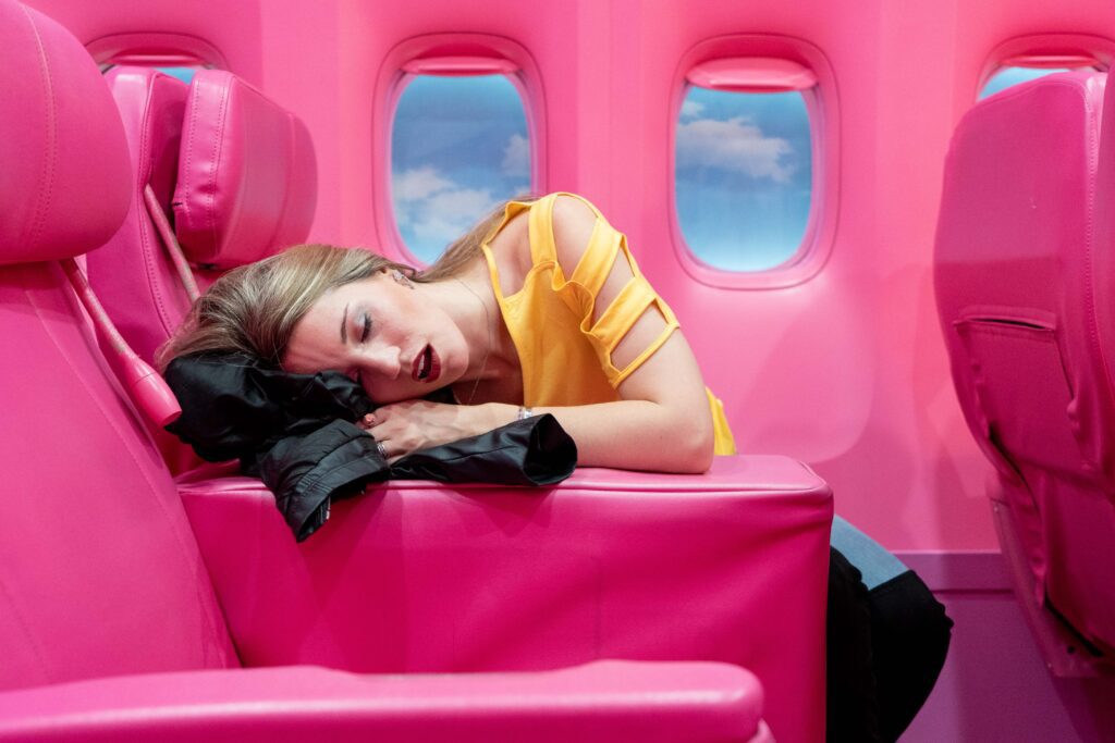 Lady sleeping uncomfortably on a pink airplane. A travel pillow is a better option for comfortable journeys