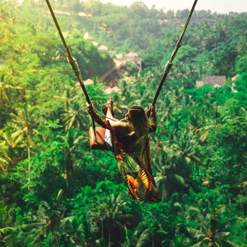 Solo travel to Bali could be an experience of a lifetime. Read our guide to learn more. Image shows an individual on a swing looking over green forestry.